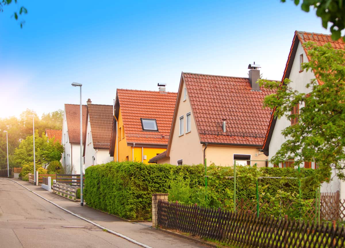 Straße mit Einfamilienhäusern mit Ziegeldächern hinter einer Hecke